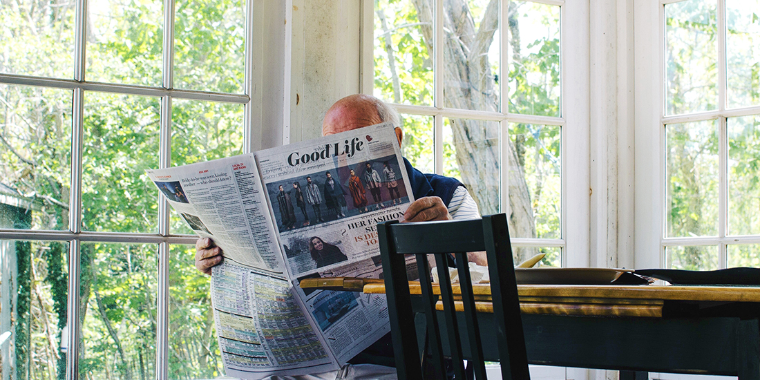 Elderly man reads a newspaper in a sunroom